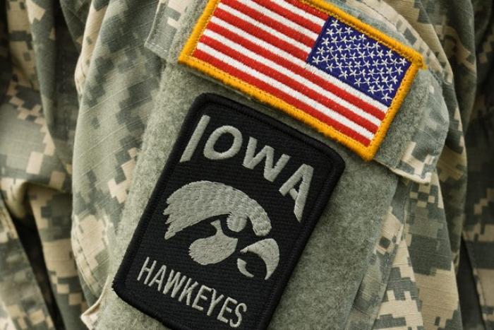 United States of America flag patch above Iowa Hawkeye logo patch on shoulder of a military uniform.